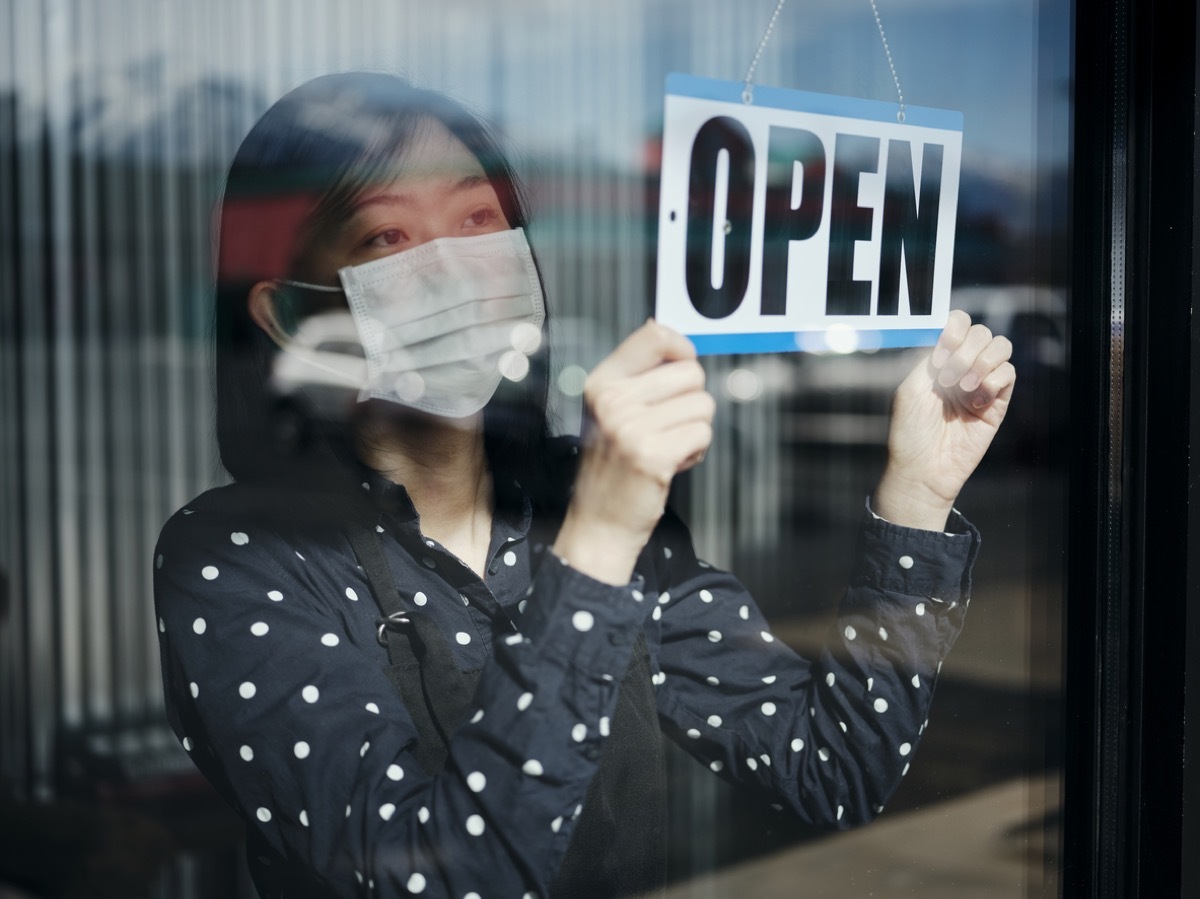 A business owner changing the store sign to OPEN after being closed for a period of time due to social distancing guidelines related to Coronavirus.