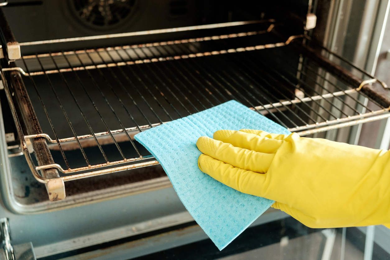 hand in yellow glove cleaning oven with blue sponge