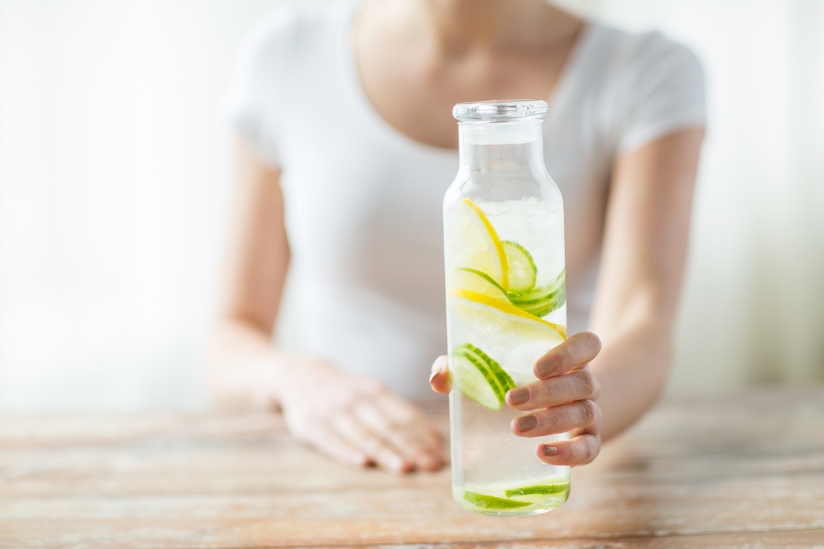 Woman holding a glass bottle of refreshing lemon and cucumber infused water