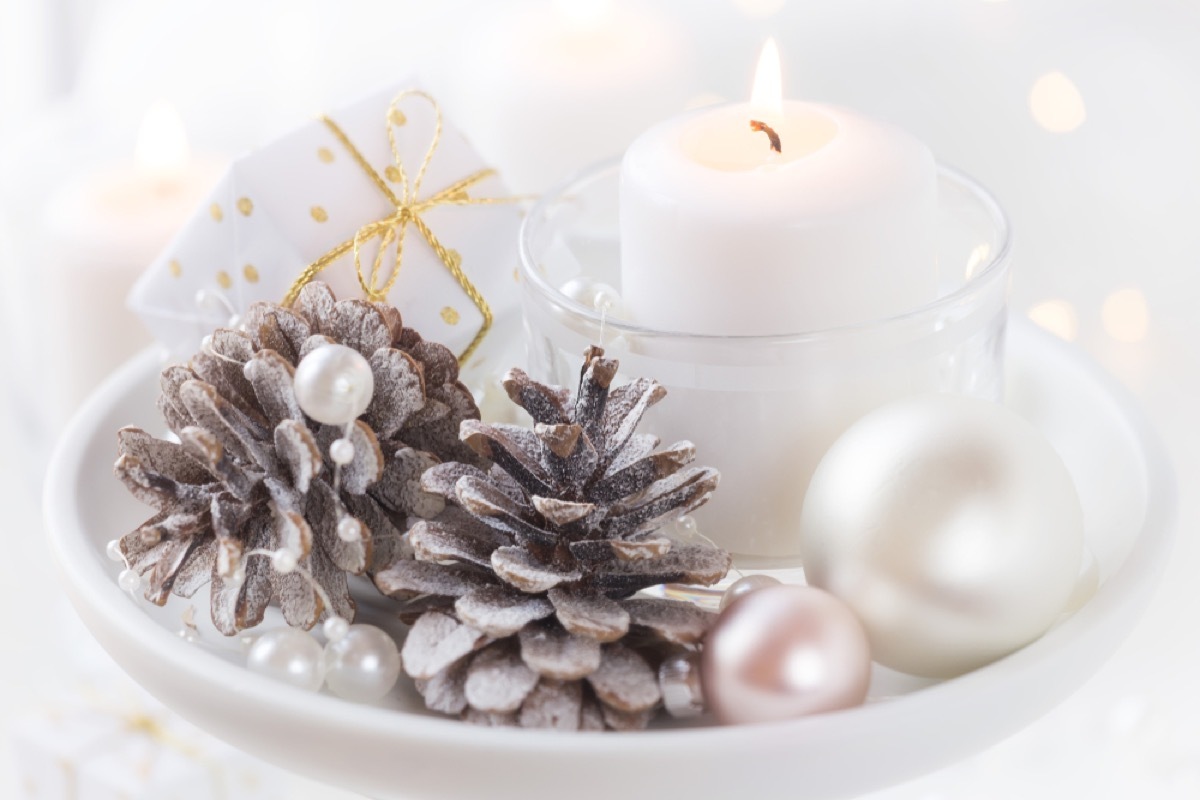 pine cones spray painted silver next to white candles in white ceramic dish