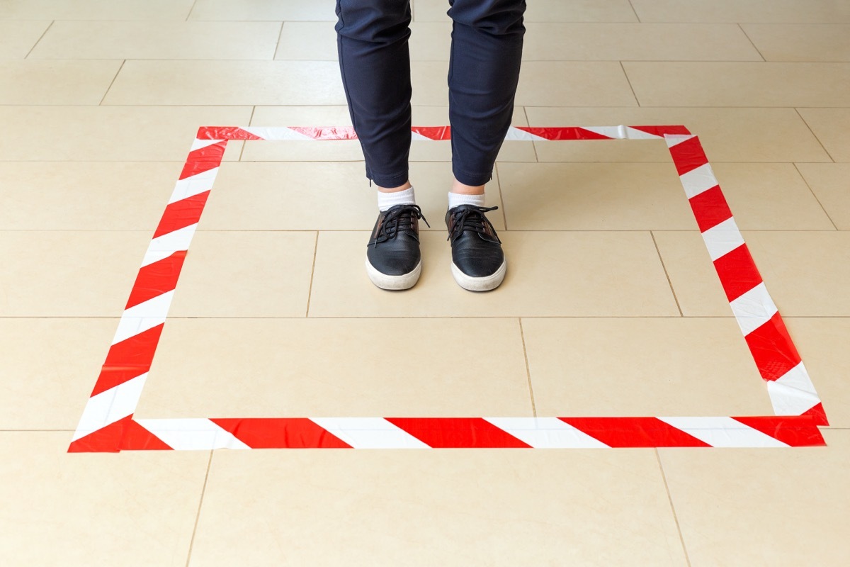 person standing in masking tape square on floor as social distancing measure in store