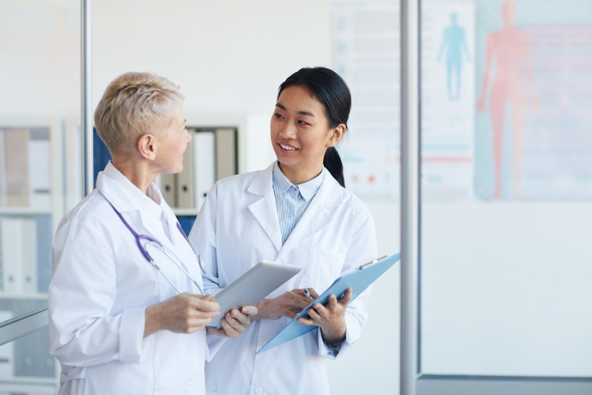 two doctors talking in hospital carrying clipboards and a tablet