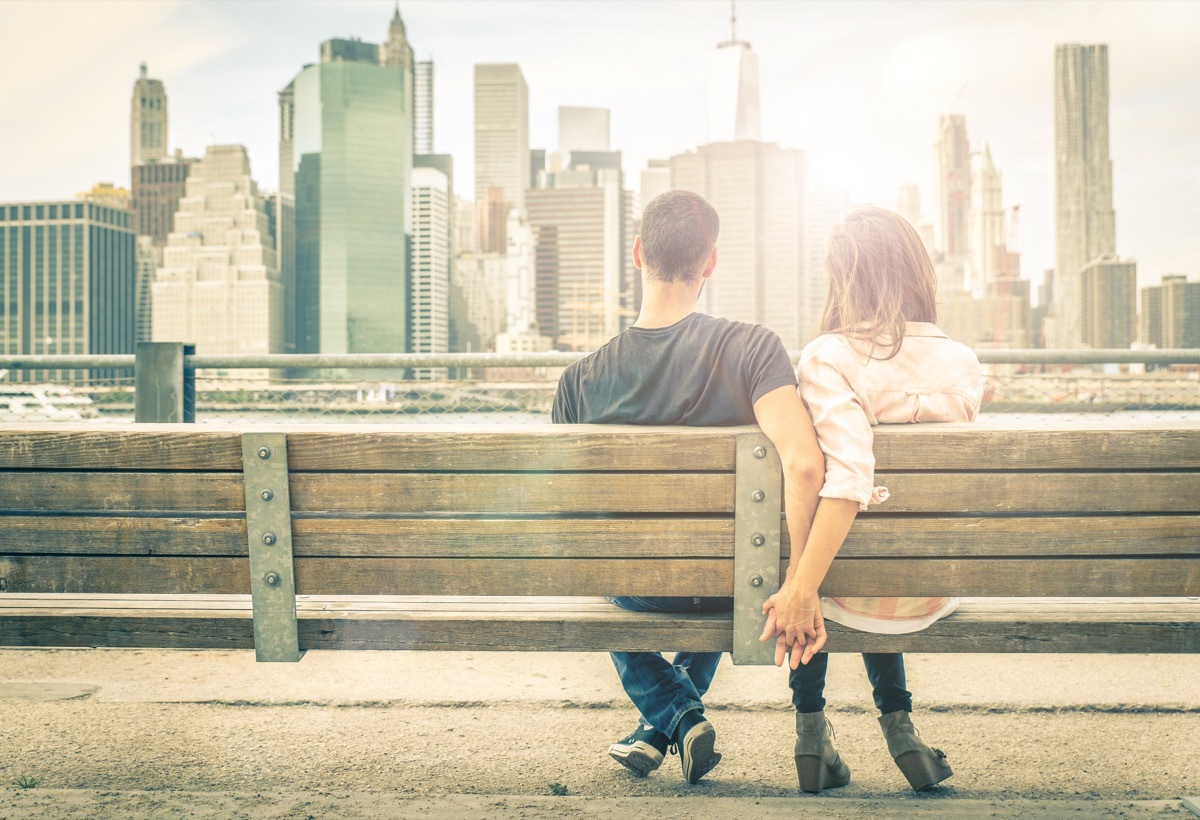 Couple holding hands on park bench looking at the city skyline