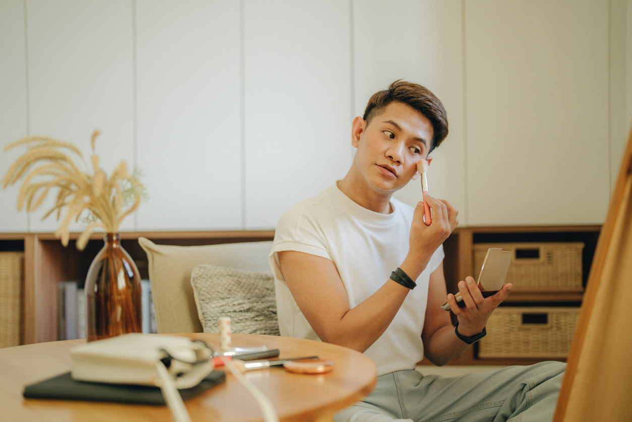 Asian non-binary gender person applying makeup in dressing room.