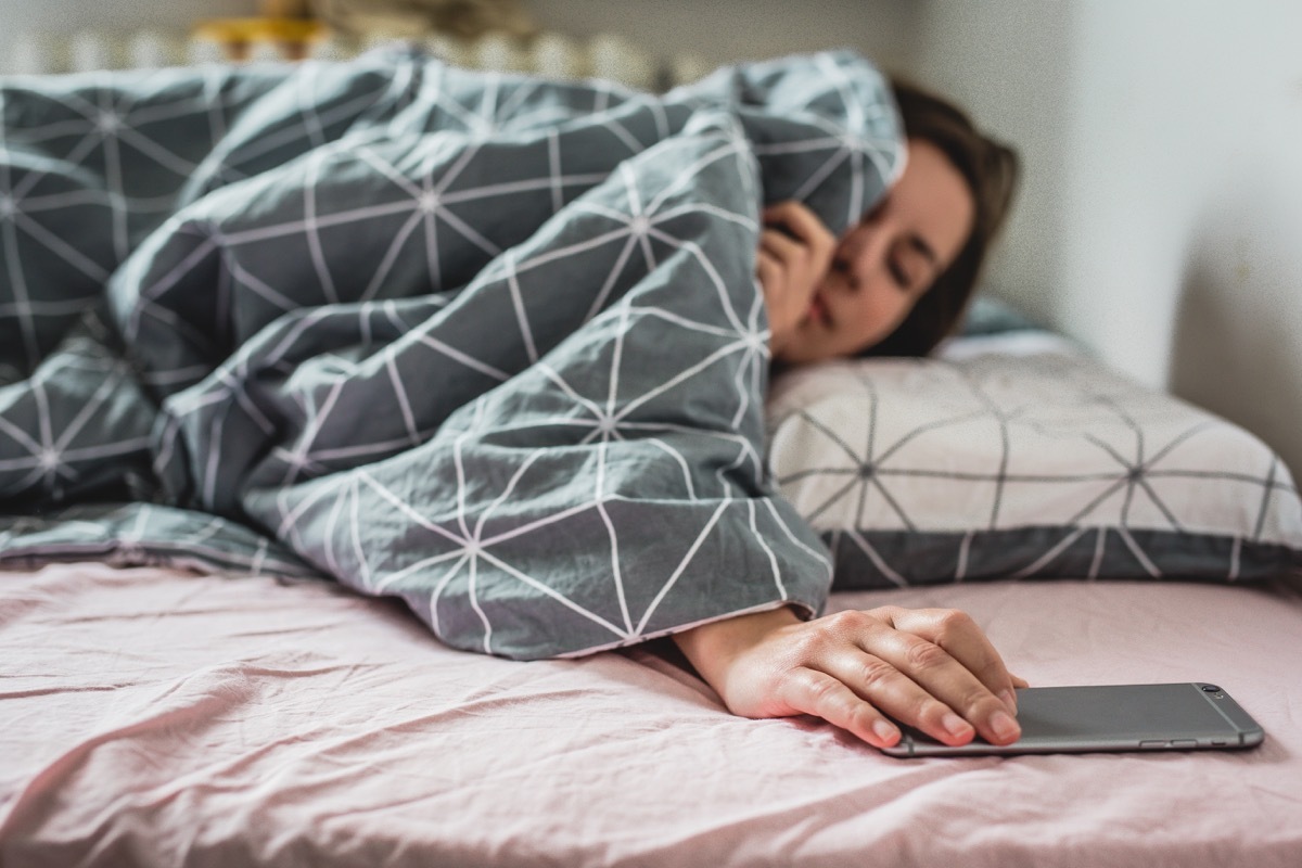 A young woman wakes up the bed. the alarm on the smartphone is ringing