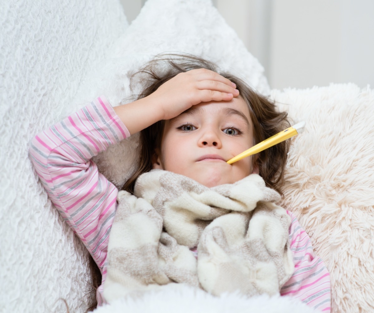 sick girl lying in bed with a thermometer in mouth and touch his forehead