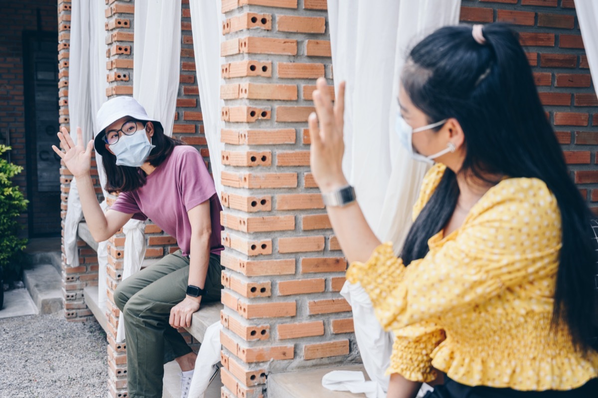 young asian women waving at each other while wearing masks