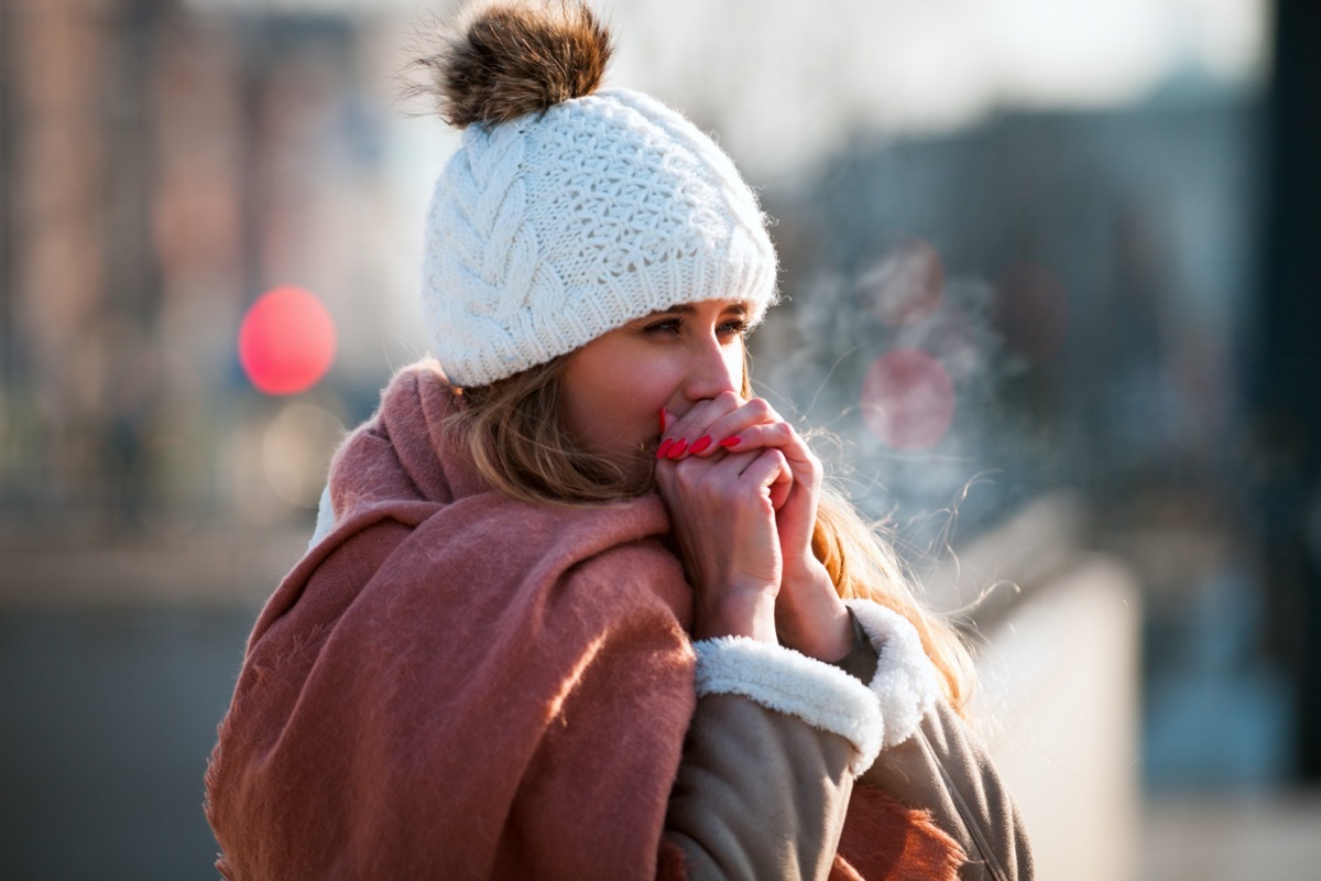 Woman breathing on her hands to keep them warm at cold winter day