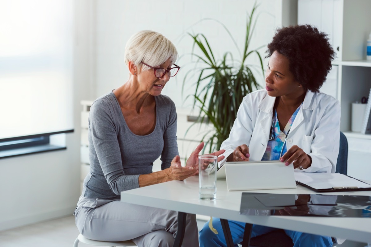 A female doctor sits at her desk and chats to an elderly female patient while looking at her test results