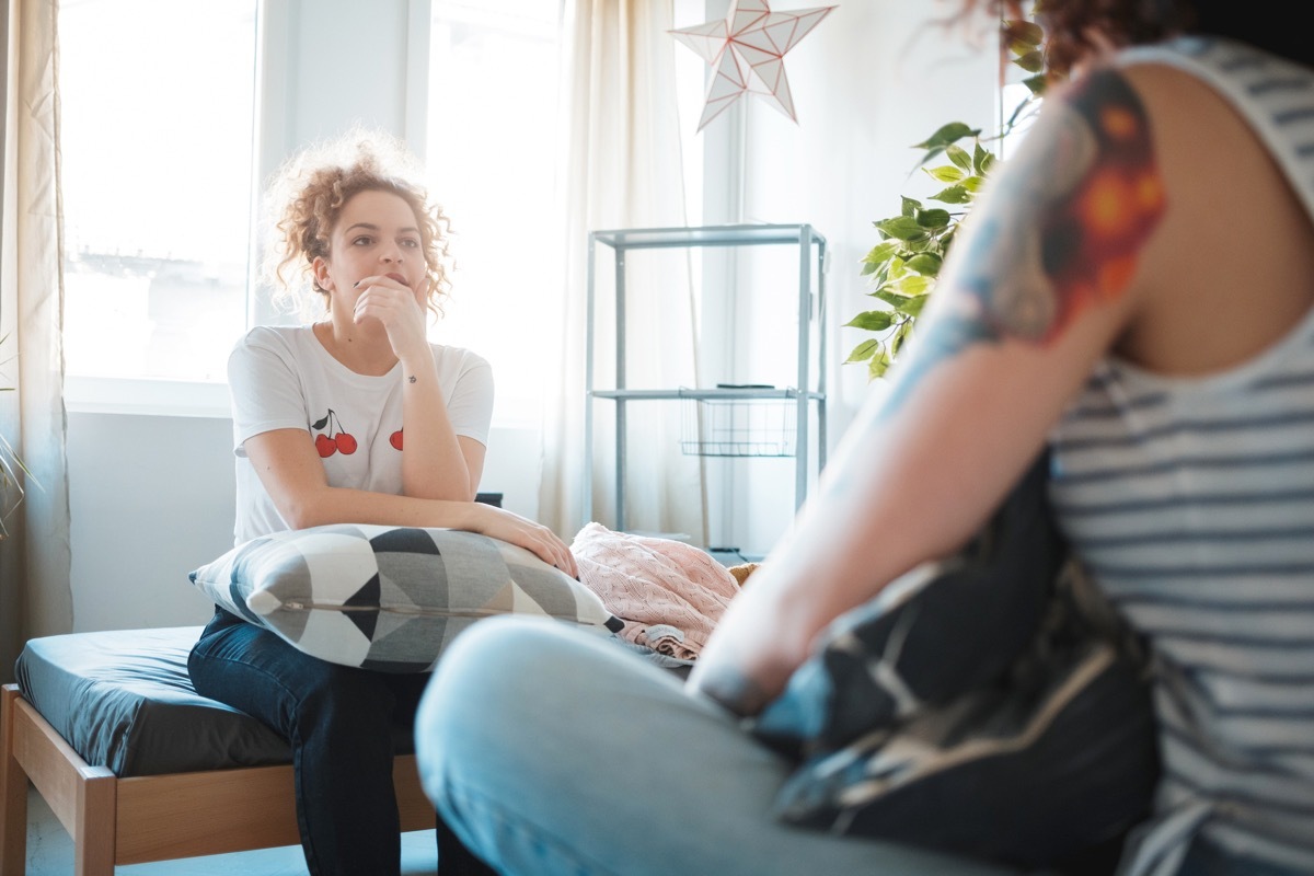 young woman sitting on the bed with hand on chin and listening carefully to her friend