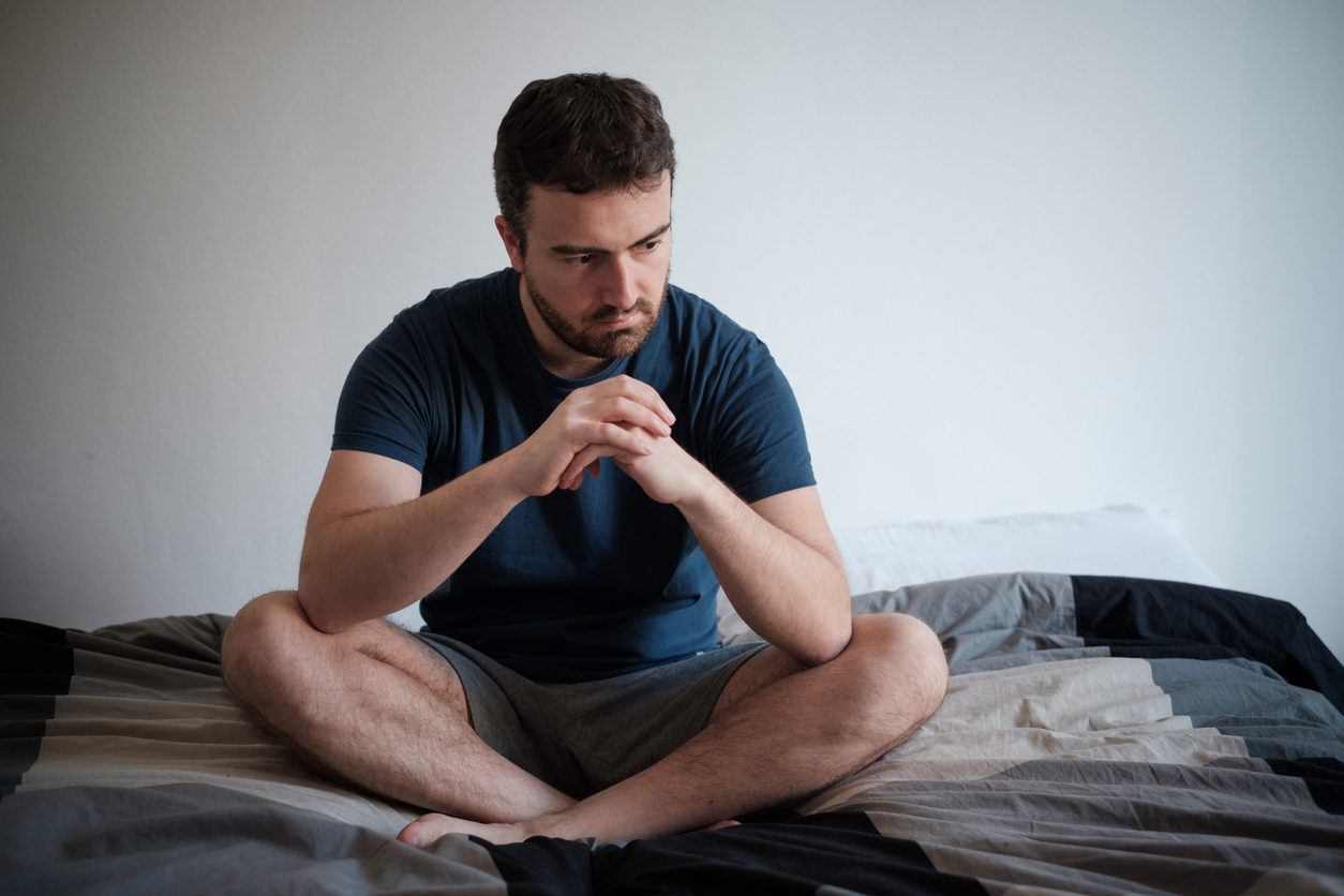 Man sitting on bed feeling sad. 