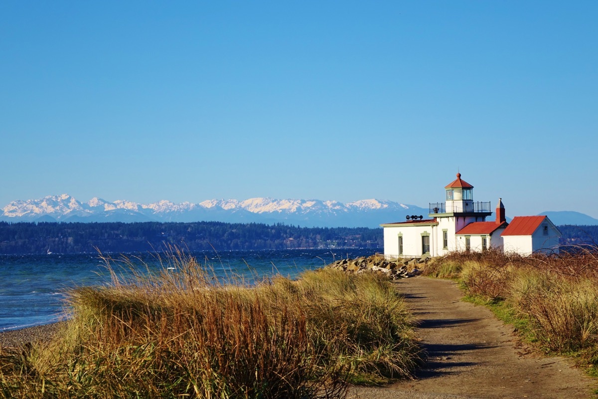 lighthouse against the water with mountains in the background