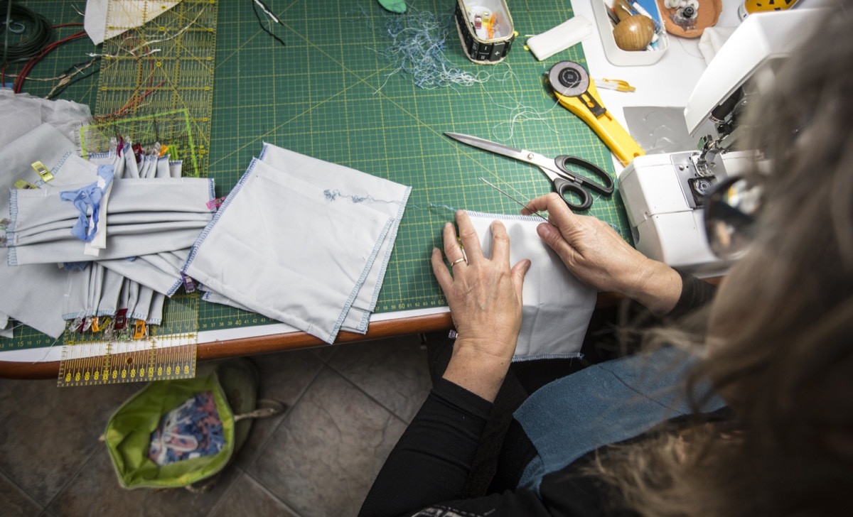 Over Shoulder View of Mature Woman Sewing Protective Face Masks at Home During Coronavirus Pandemic.