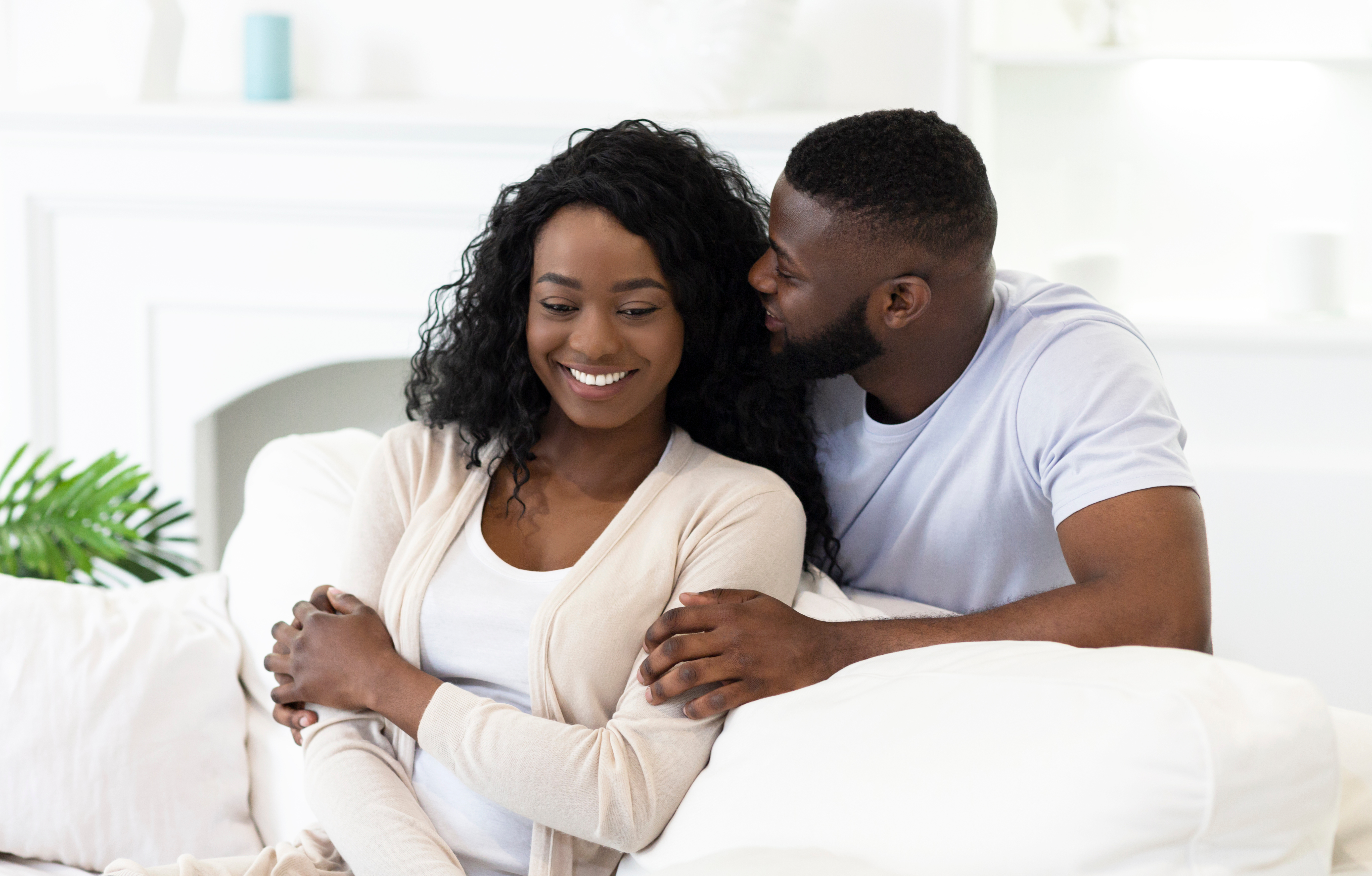 Man whispering into woman's ear in bedroom