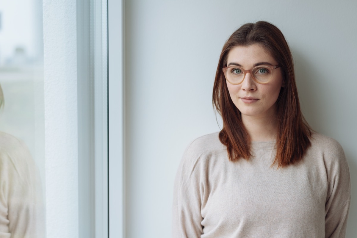 Woman with brown hair and a beige shirt standing against a white wall