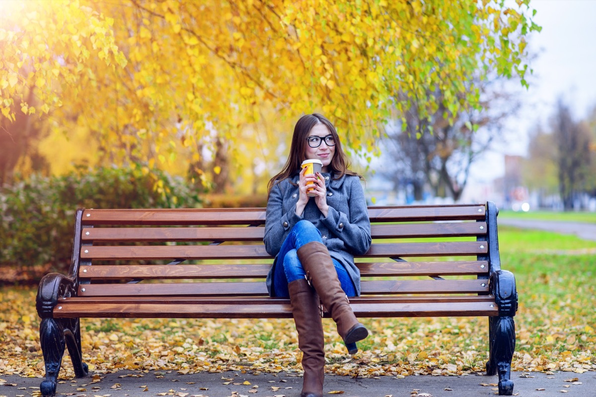 Woman drinking coffee on a park bench while people watching