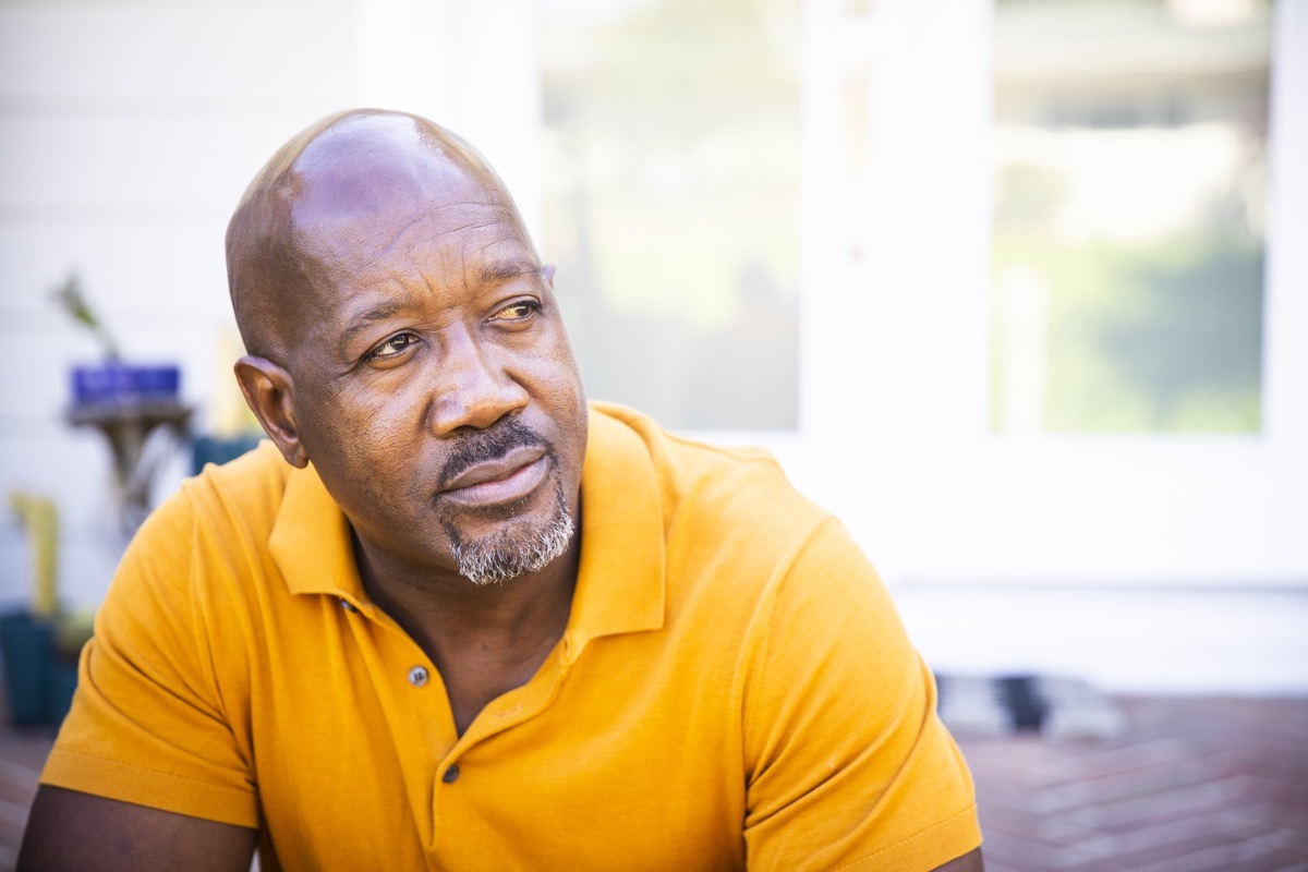 A mature black man looks out while sitting on his porch