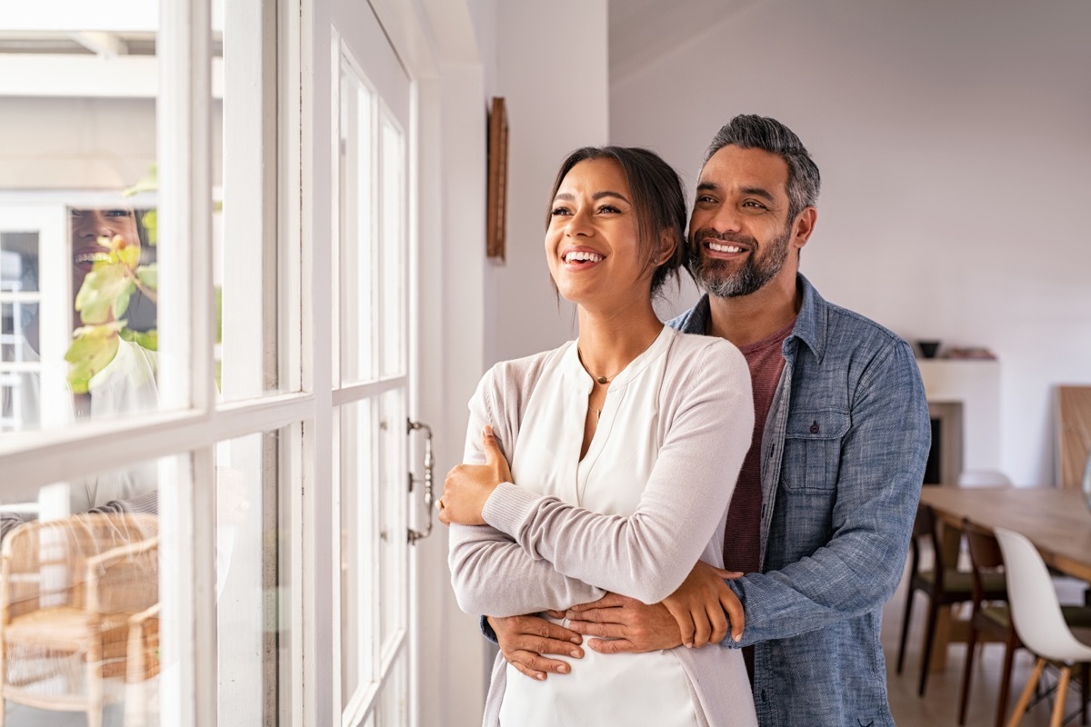 Smiling couple hugging one another looking out the window. 