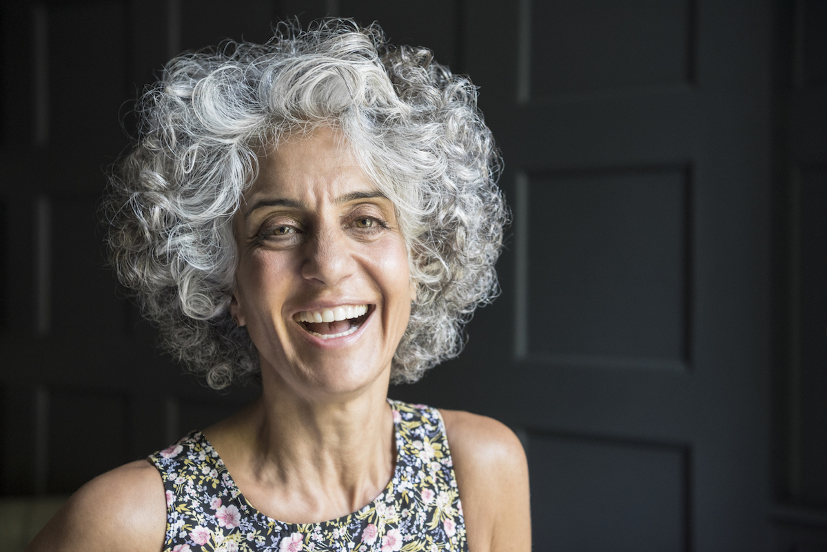 Portrait of a woman in her 50s with cheerful expression, with short curly gray hair.