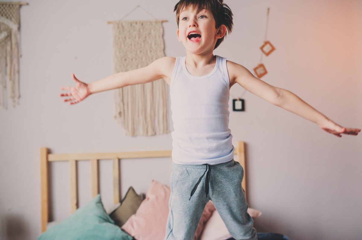 happy naughty boy jumping in bed in early morning. Hyperactive kids, casual lifestyles.