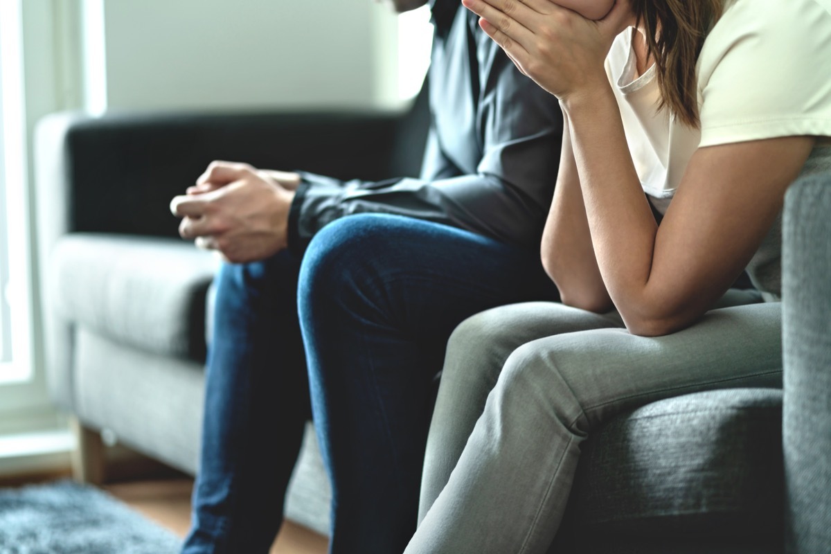 cropped image of couple sitting on couch, woman with face in her hands