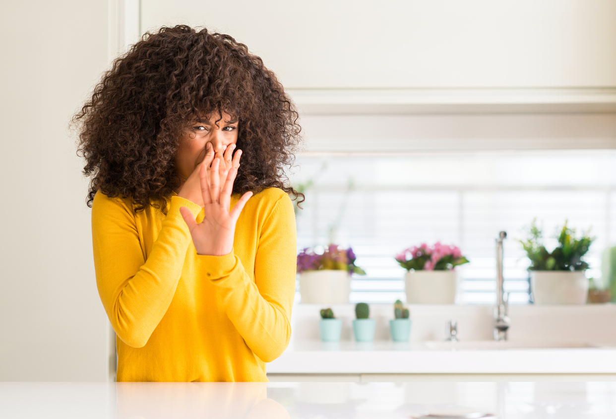 African american woman wearing yellow sweater at kitchen smelling something stinky and holding her nose