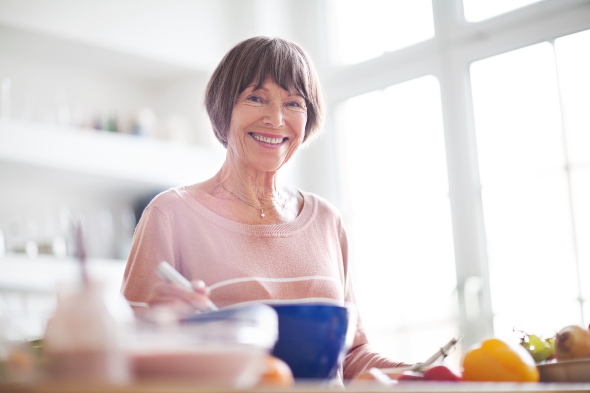 Elderly woman in kitchen looking at camera smiling.