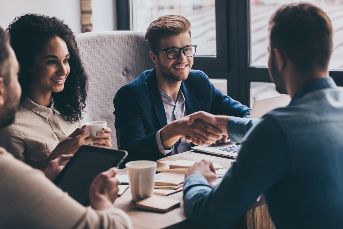 man shaking hands with bosses across a conference room - how to ask for a promotion