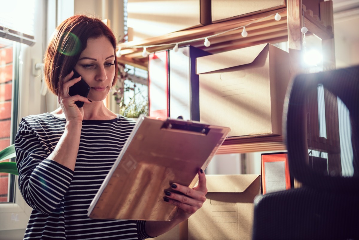 Business woman wearing striped shirt talking on the phone at the office and looking at document