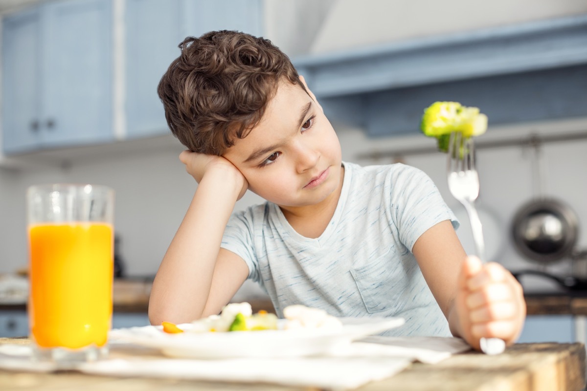 Young boy looking at broccoli avodiing eating at dinner 