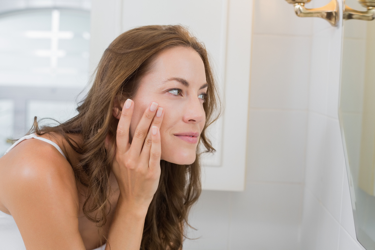 Side view of a woman examining her face in the mirror in the bathroom at home