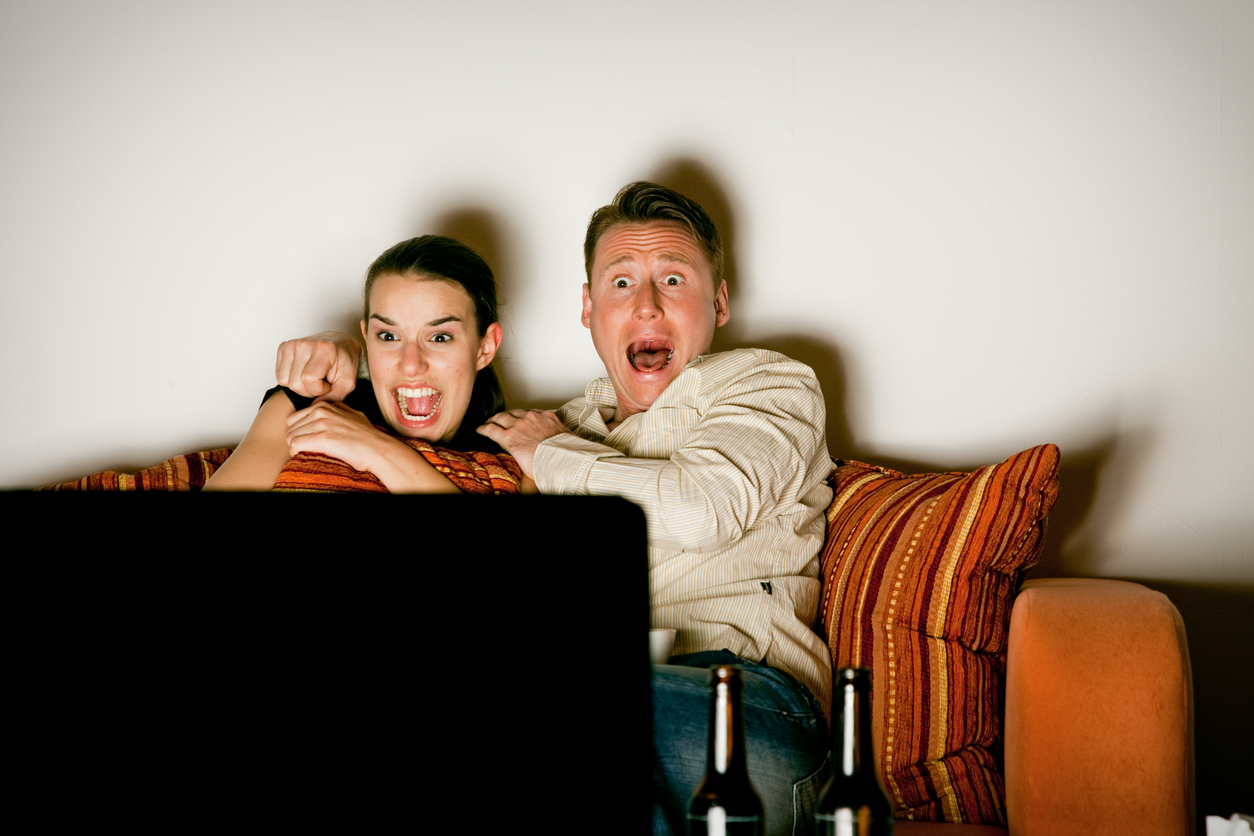 a couple is sitting on a couch and watching a VERY scary movie scene on tv.