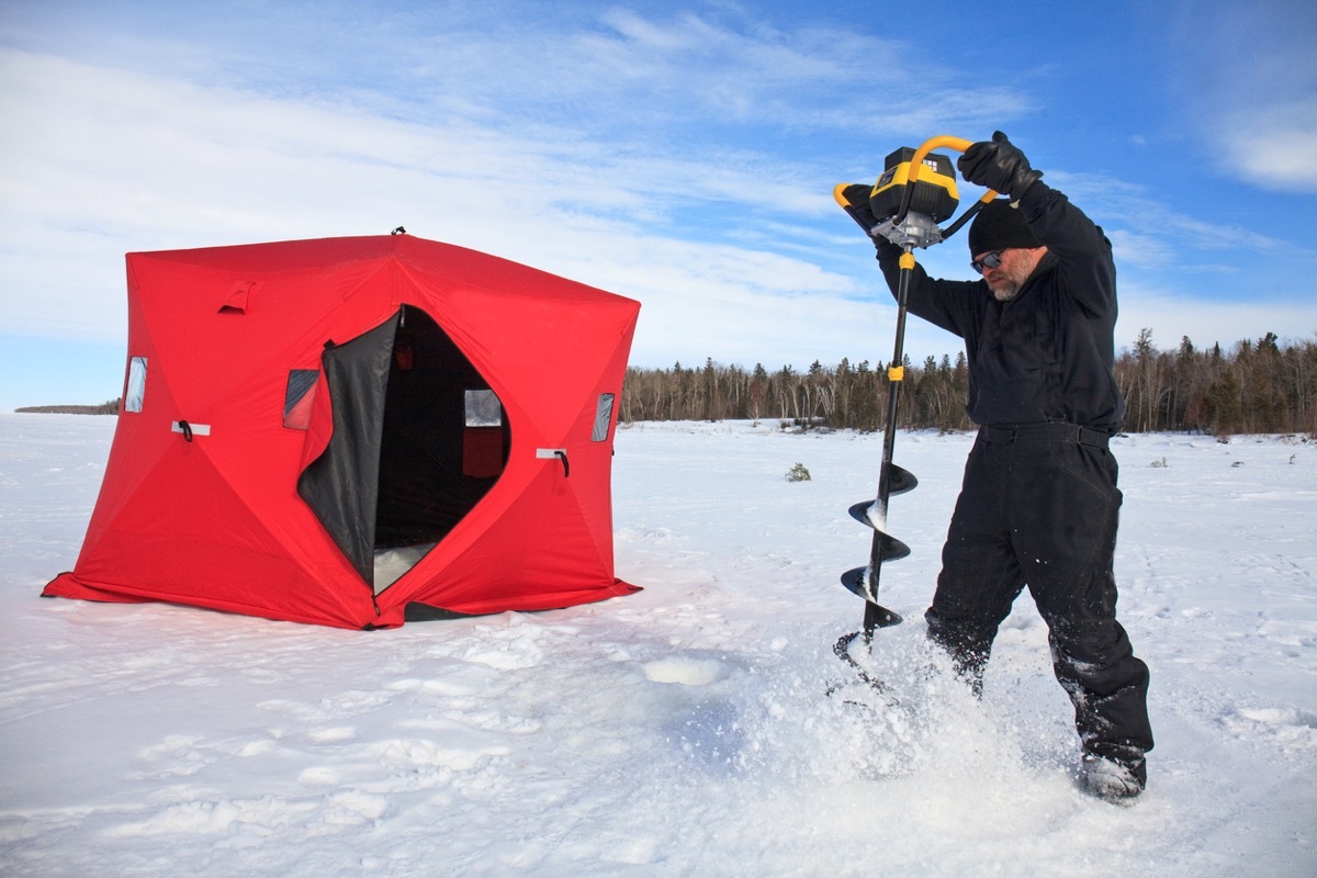 A man drilling a hole with an ice auger for ice fishing expedition in Manitoba, Canada.