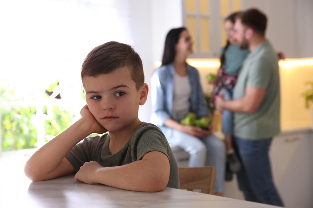 Unhappy little boy feeling jealous while parents spending time with his sister at home