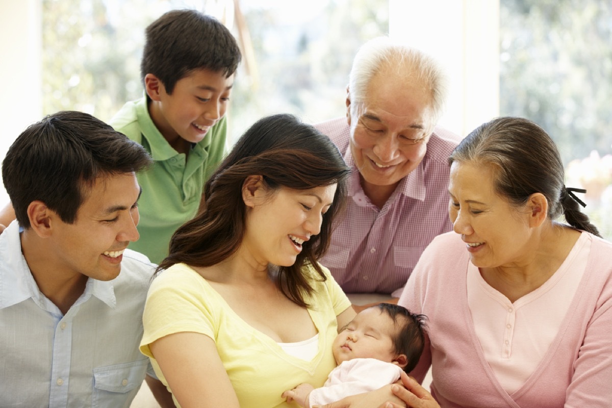 asian family looking at woman holding new baby