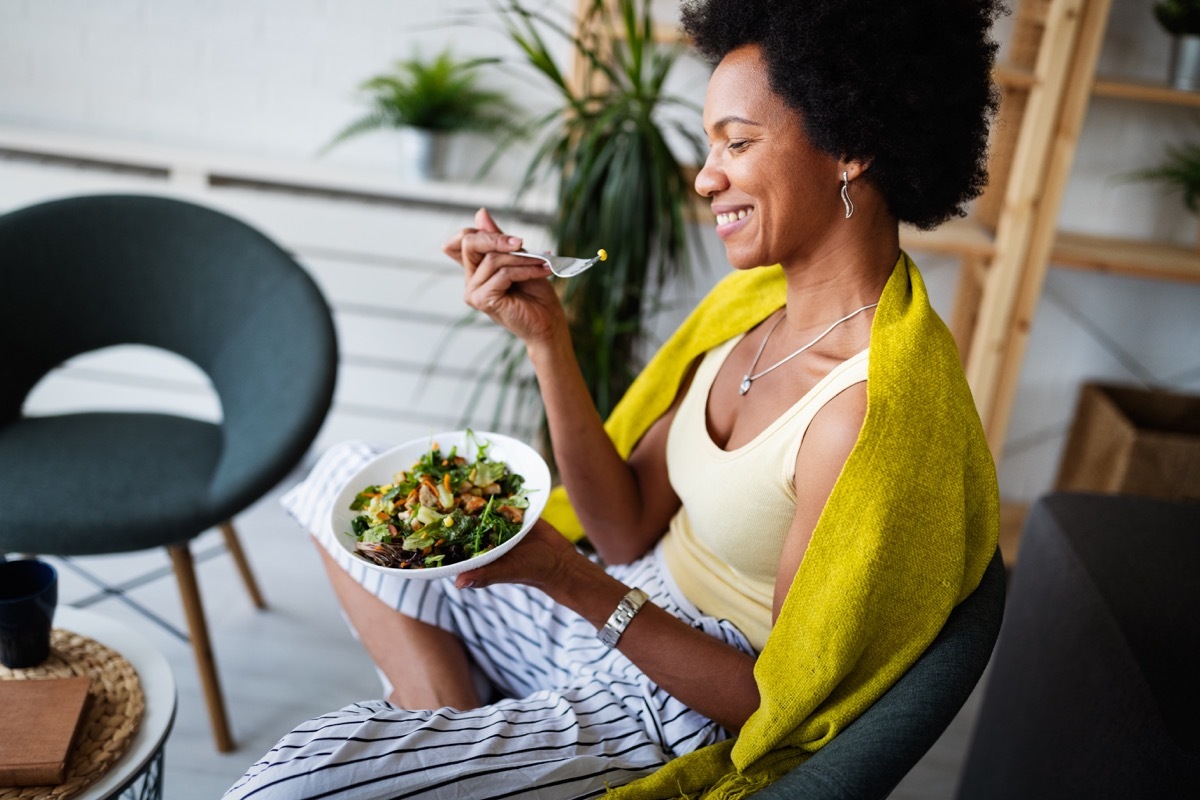 woman, sitting with bowl of salad, eating, smiling