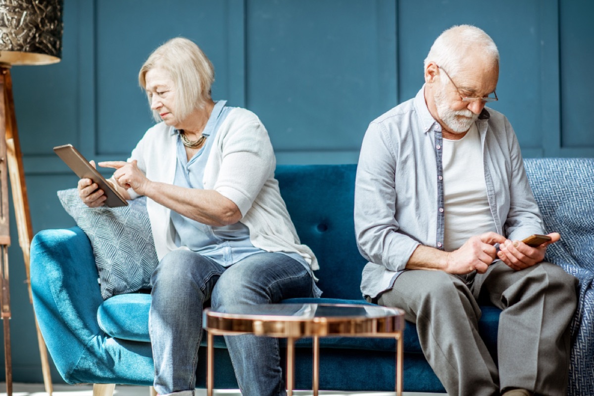 older couple ignoring each other on couch using smartphone and tablet, etiquette mistakes