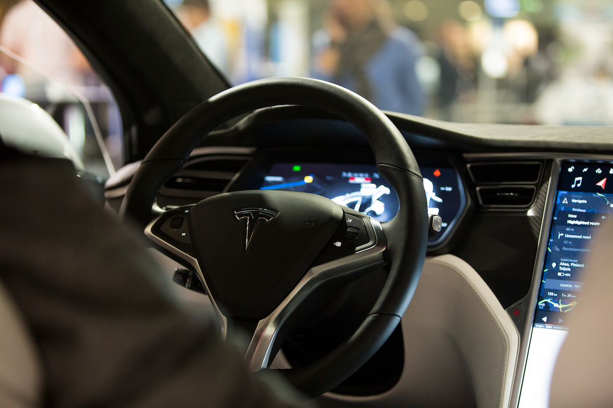 The interior of a Tesla Model X electric car with large touch screen dashboard, wheel.