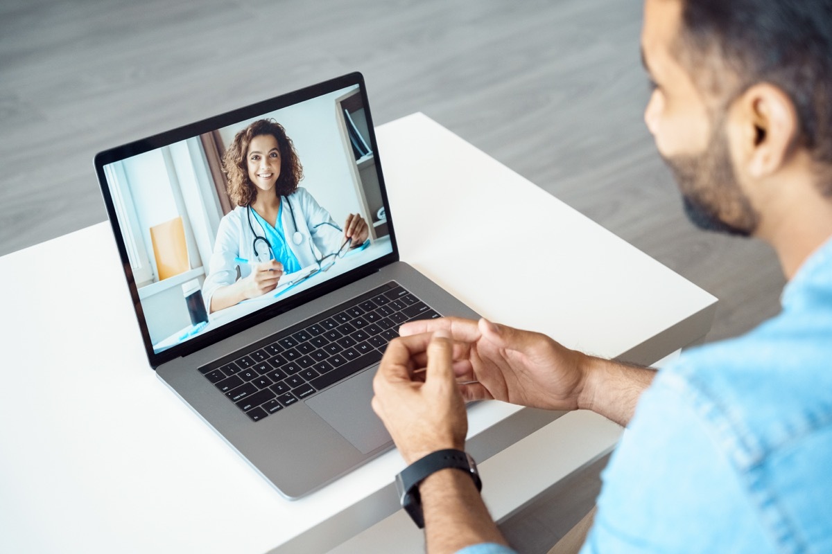 View over a man's shoulder as he does a tele-health appointment with a female doctor on his laptop