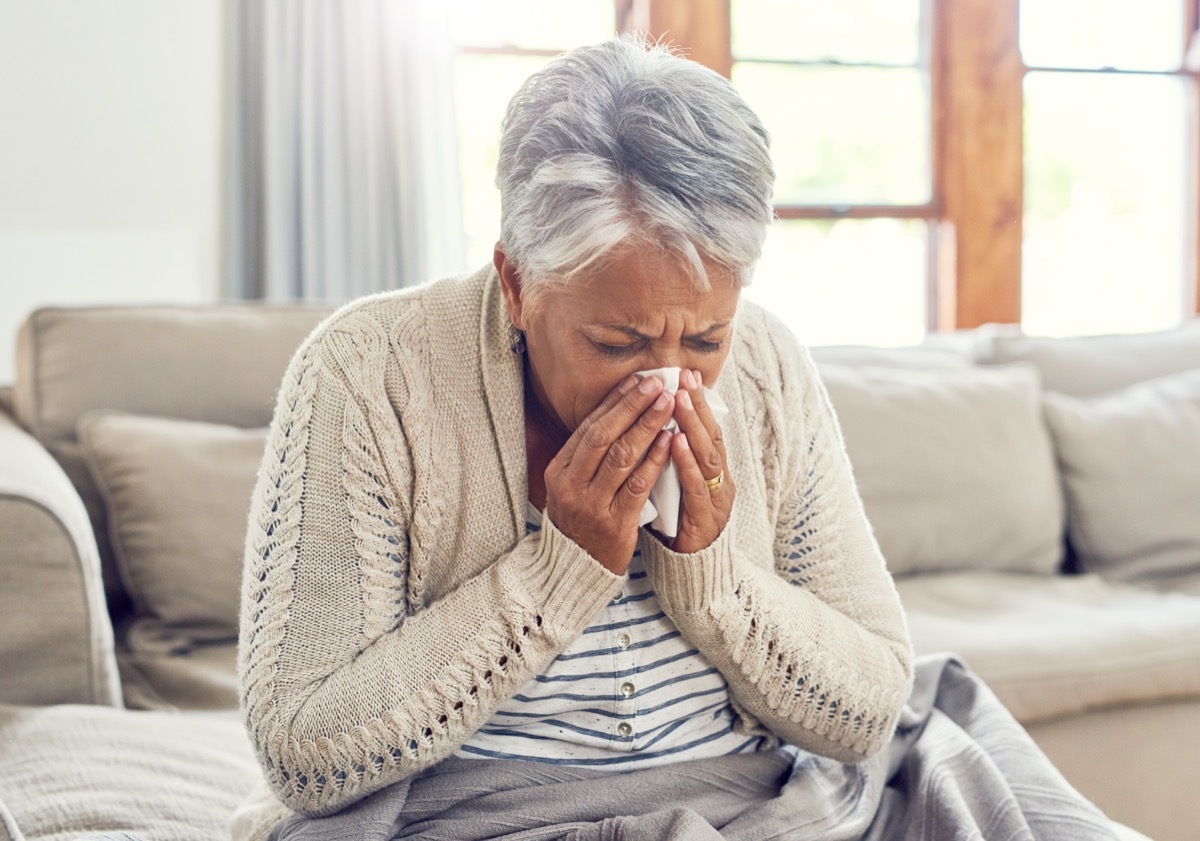 Shot of a sickly senior woman blowing her nose with a tissue while sitting on a sofa ta home