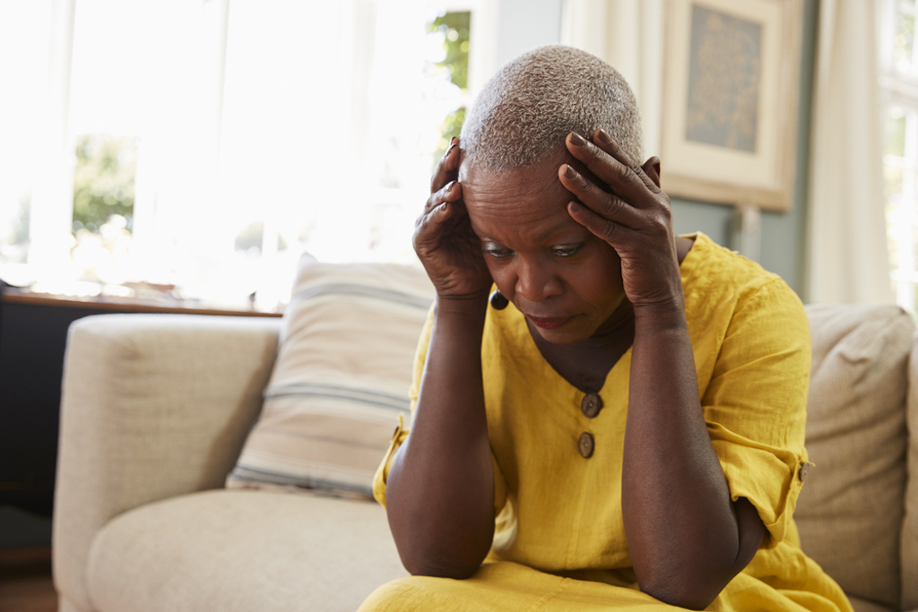 woman, holding head while sitting on couch, has dementia