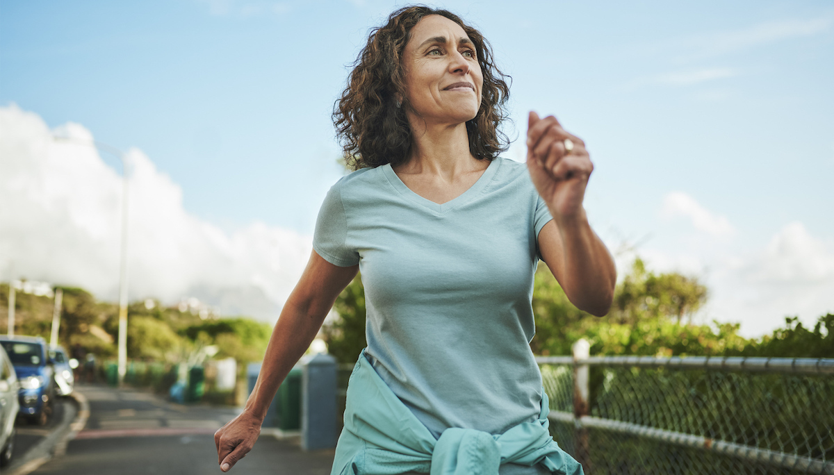 Mature woman in seafoam green sportswear smiling while out for a power walk in summer