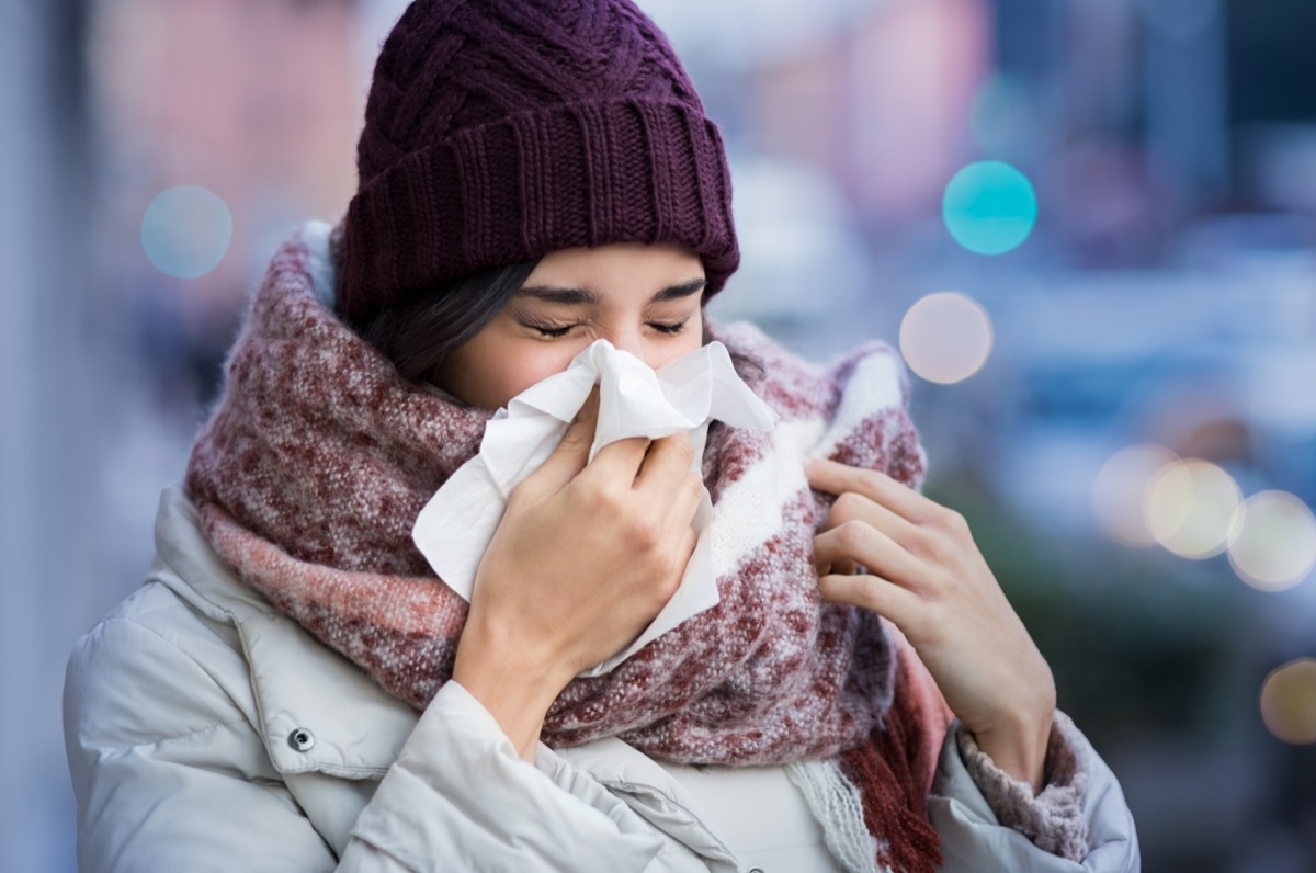 young woman blowing her nose outdoors