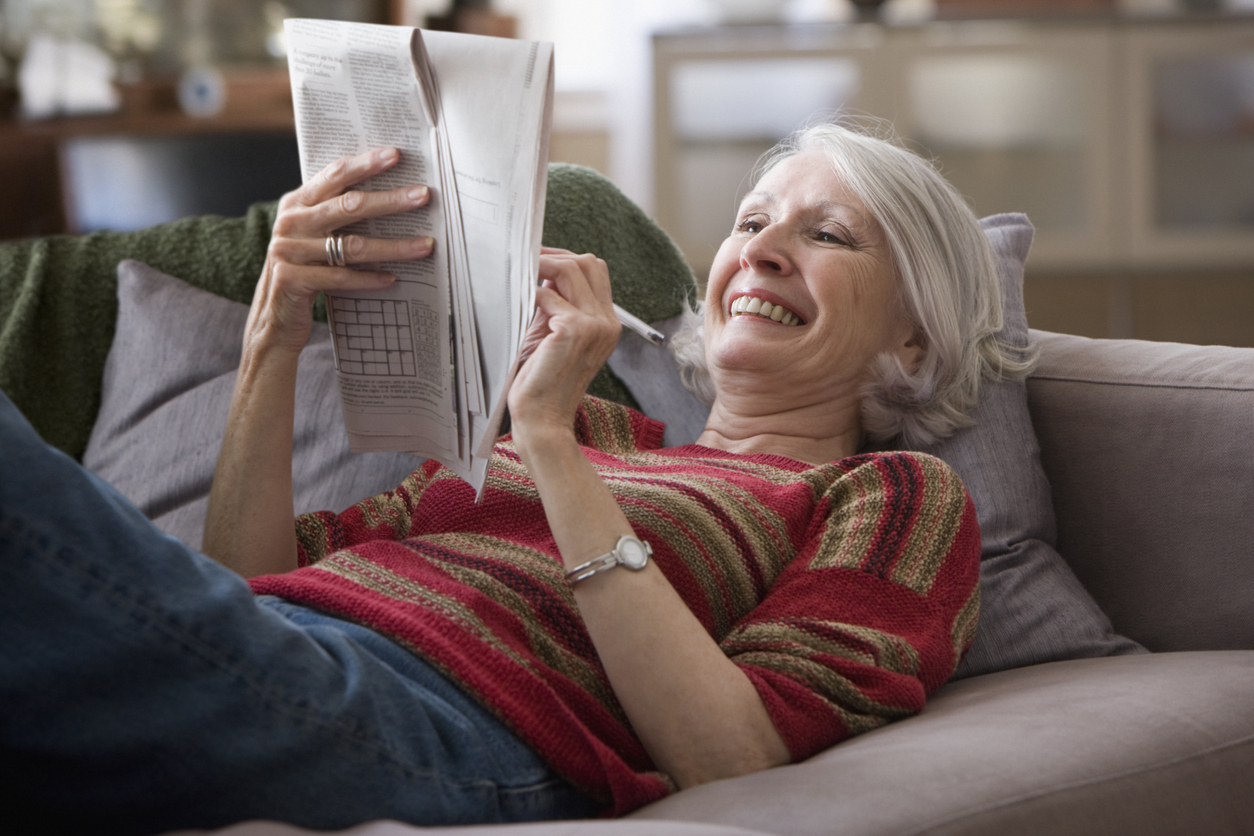 Woman lying on the couch doing a crossword puzzle.