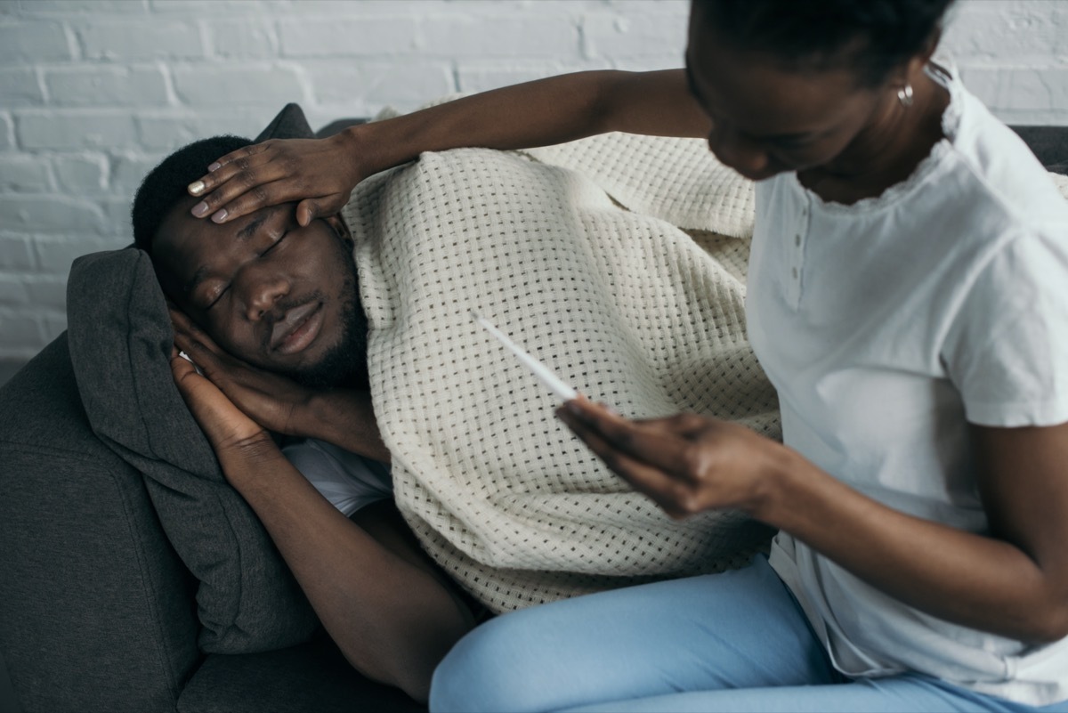 woman holding thermometer and checking forehead of sick boyfriend.