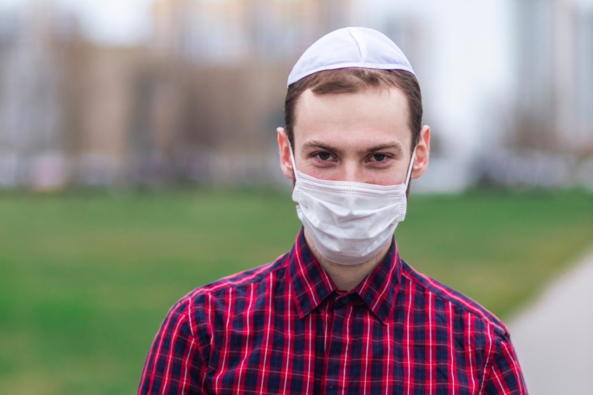 Young Jewish man in traditional jewish male headdress, wearing face mask outdoor.