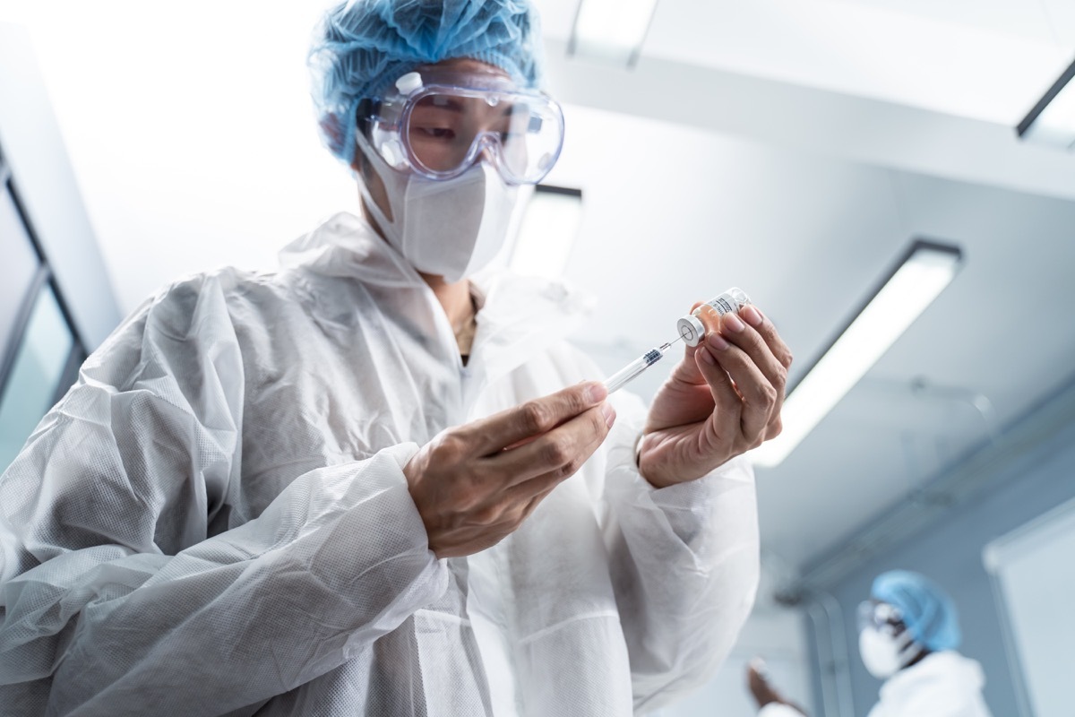 young male doctor wearing white gown, holding hypodermic syringe and vaccine in test lap for cure coronavirus for mankind in future.