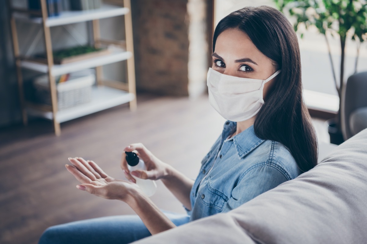 Woman wearing safety mask using disinfection spray.