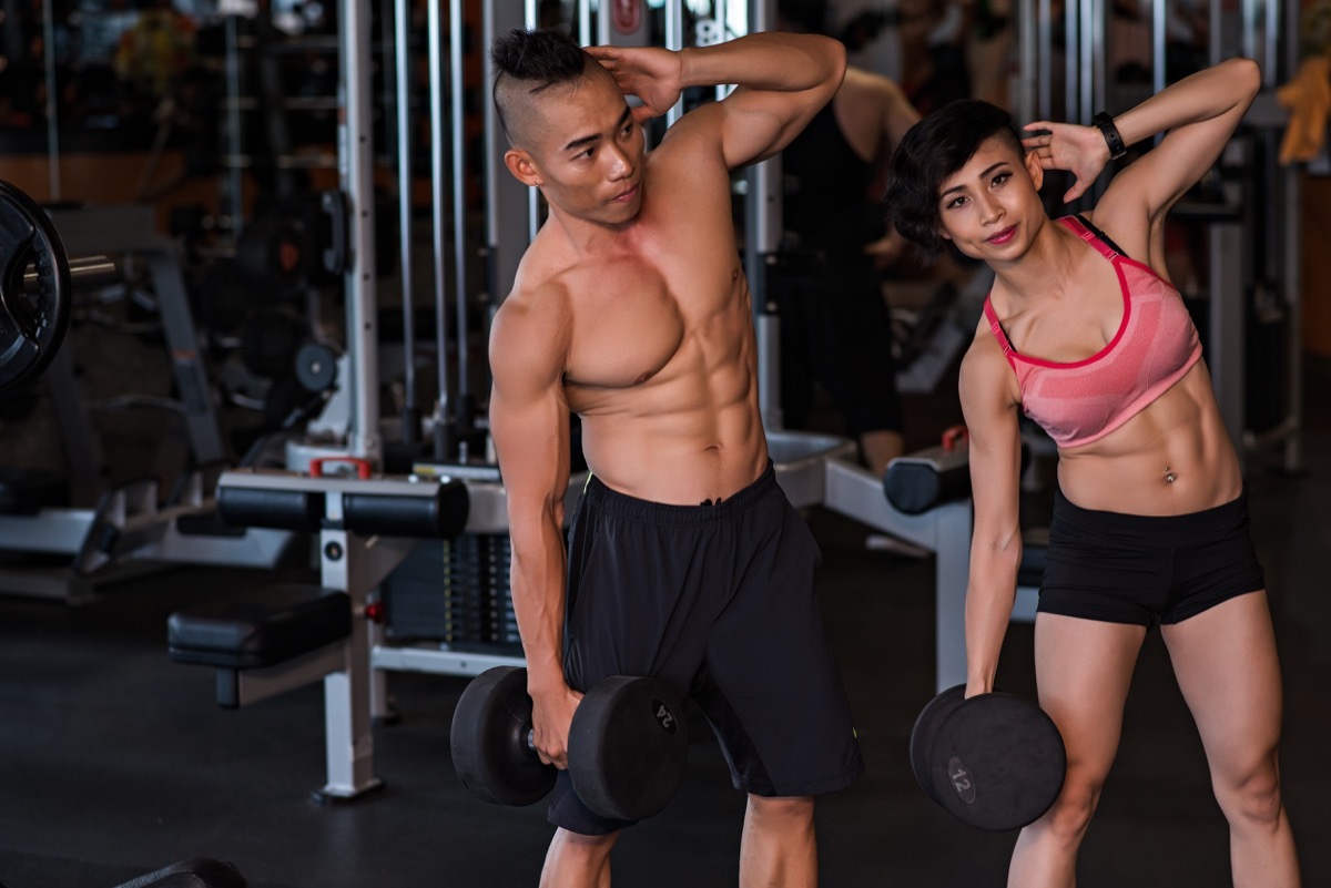 Fit couple doing dumbbell side bends at the gym