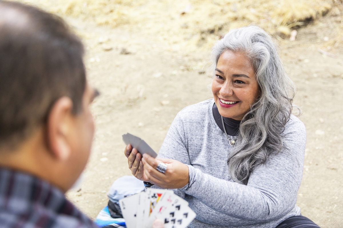 A senior latinx couple enjoying a picnic on a blanket in the woods and playing cards